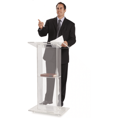 Man speaking behind the lectern with a book on the shelf, and a paper in his hand.